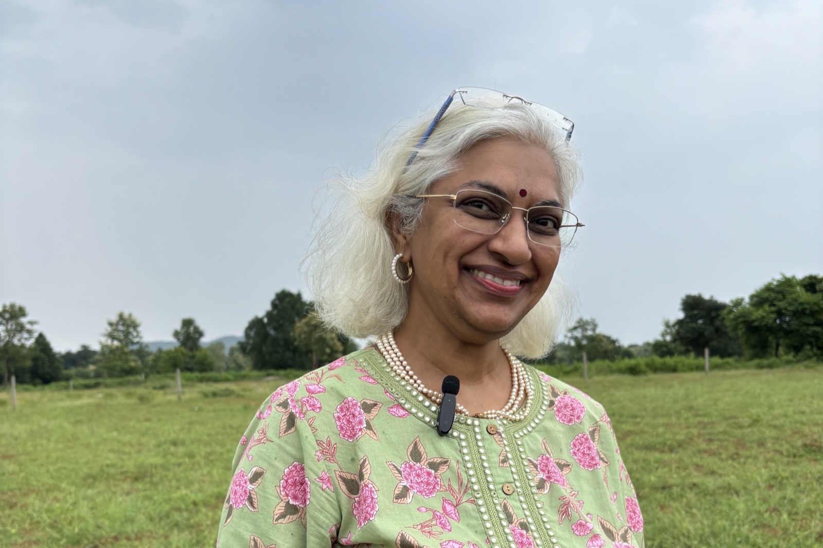 Sowmya Ayyar smiling in a green floral kurta, standing in an open green field