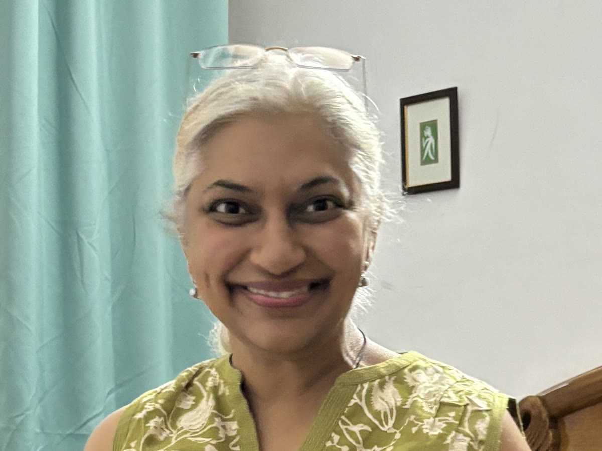 Sowmya Ayyar smiling in a green floral kurta with reading glasses resting on her head
