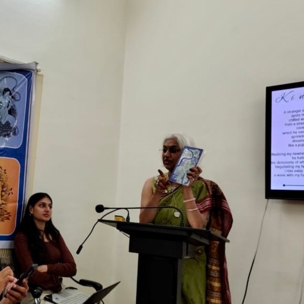Sowmya reading a poem at the launch podium, the verse projected behind her